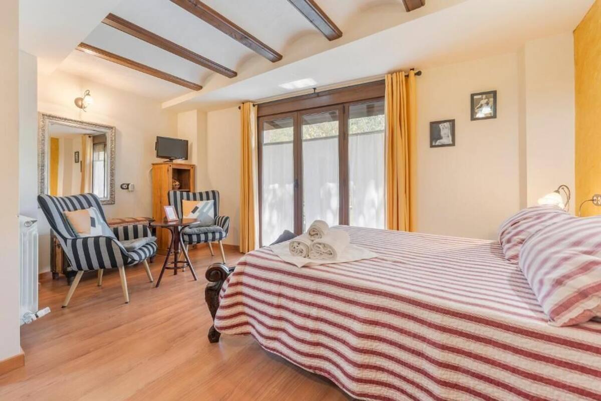 A bedroom with a bed, striped curtains, a desk with a chair, a television, and a mirror.