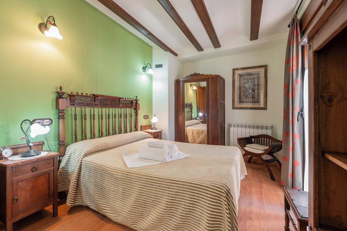 A bedroom with a bed, nightstands, a mirror, and a wooden chair.