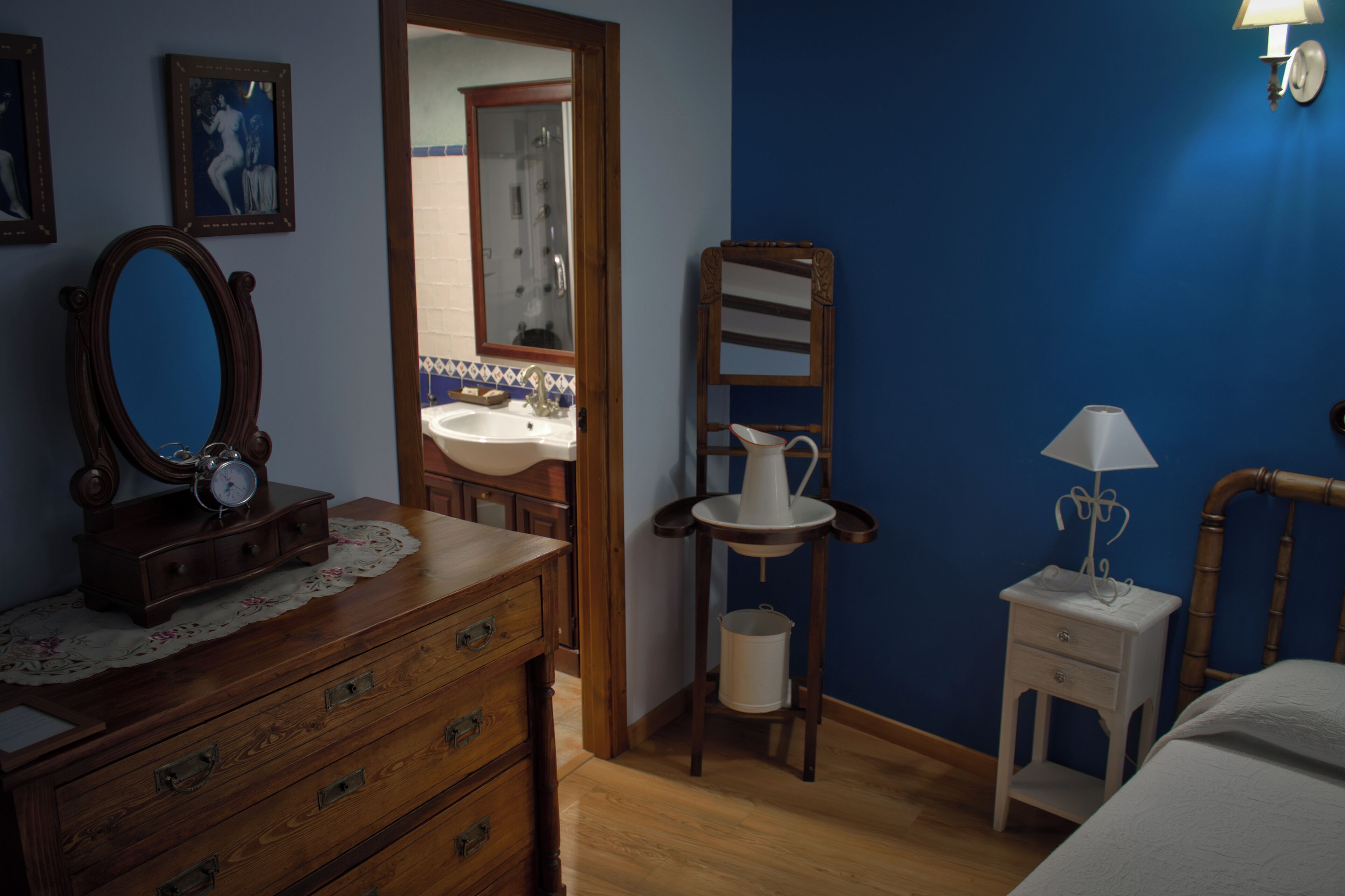 A bedroom with a wooden dresser, a mirror, a bedside table with a lamp, and a nightstand.