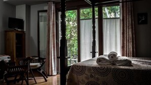 A room with a bed, a desk, and a chair. There is a window with curtains and a view of trees outside.