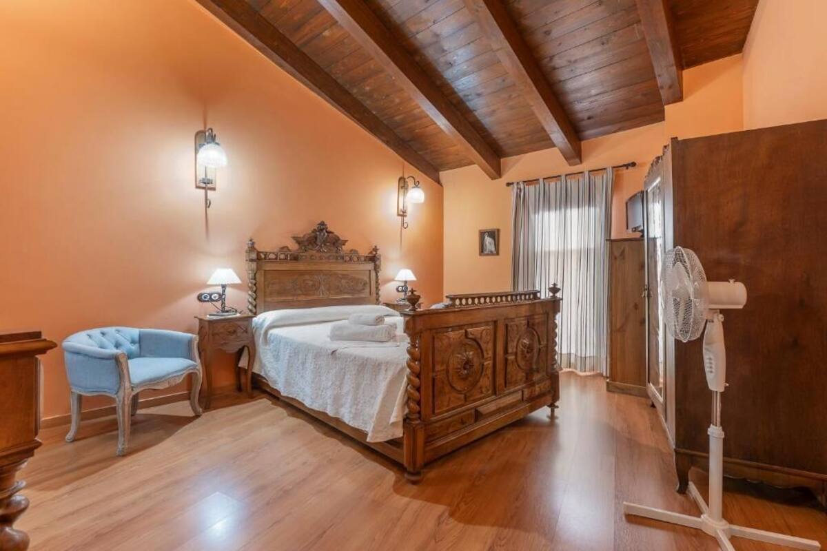 A bedroom with a wooden bed, a chair, a nightstand, and a fan.