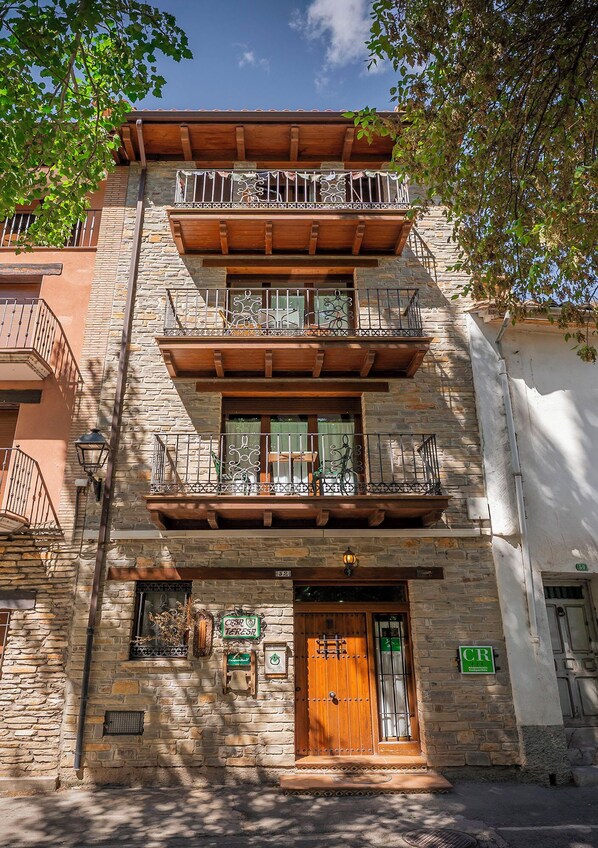 Un immeuble à plusieurs étages doté d’un balcon en bois, d’une façade en pierre et d’une enseigne verte indiquant la présence d’un restaurant.