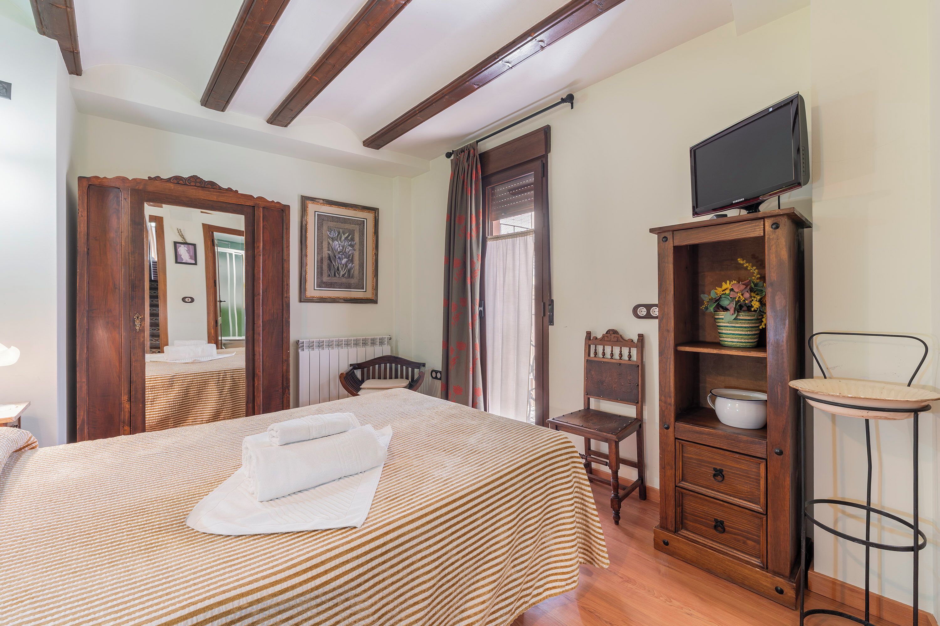 A hotel room with a bed, a television on a wooden stand, a wooden cabinet with a bowl, and a chair.