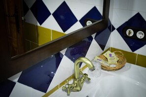 A bathroom with a gold faucet, a mirror, and a tiled wall with blue and yellow patterns.