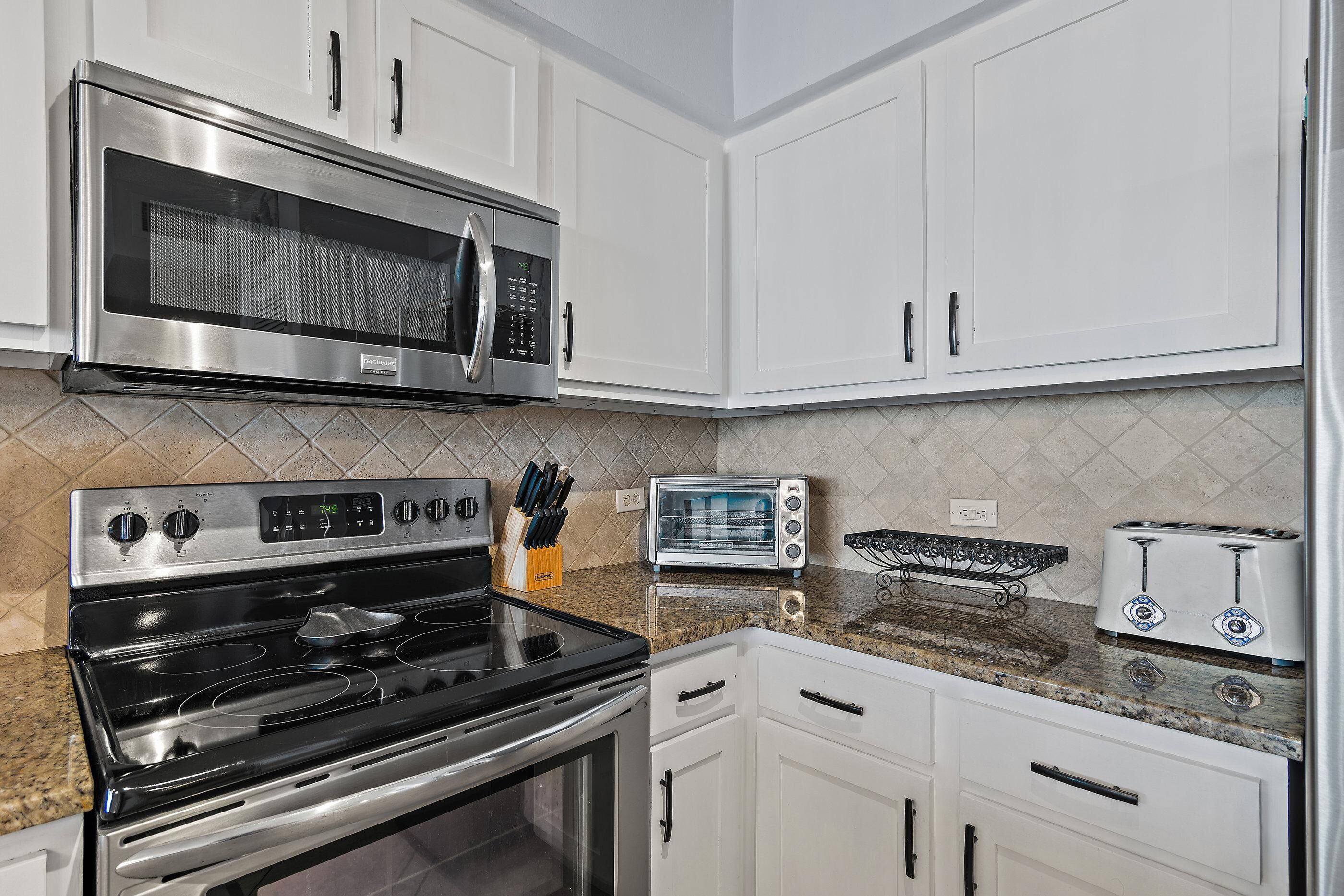 A kitchen with white cabinets, a stainless steel microwave, a toaster, and a stove.