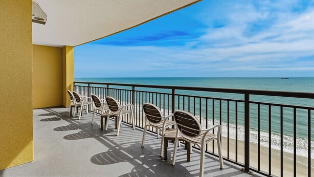 Een balkon met witte plastic stoelen en uitzicht op de oceaan.