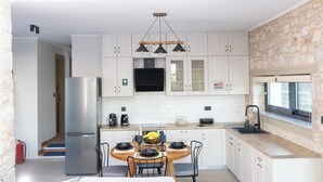 Een moderne keuken met witte kasten, een ingebouwde oven, een koelkast, een eettafel met stoelen en een accentmuur van steen.