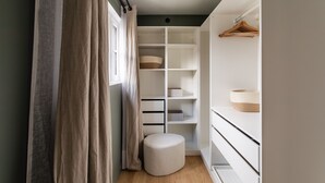 En walk-in-garderob med öppna hyllor, en klädstång och en rund sittpall.