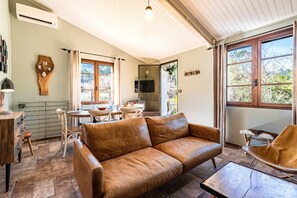 Ein Wohnzimmer mit einer braunen Ledersofa, einem Holztisch, einem Essbereich mit Tisch und Stühlen sowie großen Fenstern mit Vorhängen.