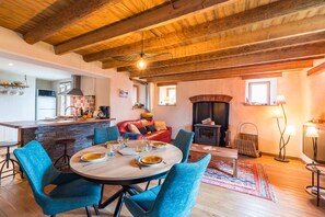 A dining area with a wooden table and blue chairs, a kitchen with a microwave and refrigerator, a fireplace, and a cozy living space with a red sofa. - An Ti Bihan - 500 m de la plage (Plougrescant)