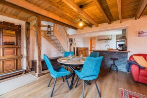 Un vaste espace de vie doté d’un plafond en bois, d’une table à manger avec des chaises bleues, d’un canapé rouge et d’une cuisine en arrière-plan.