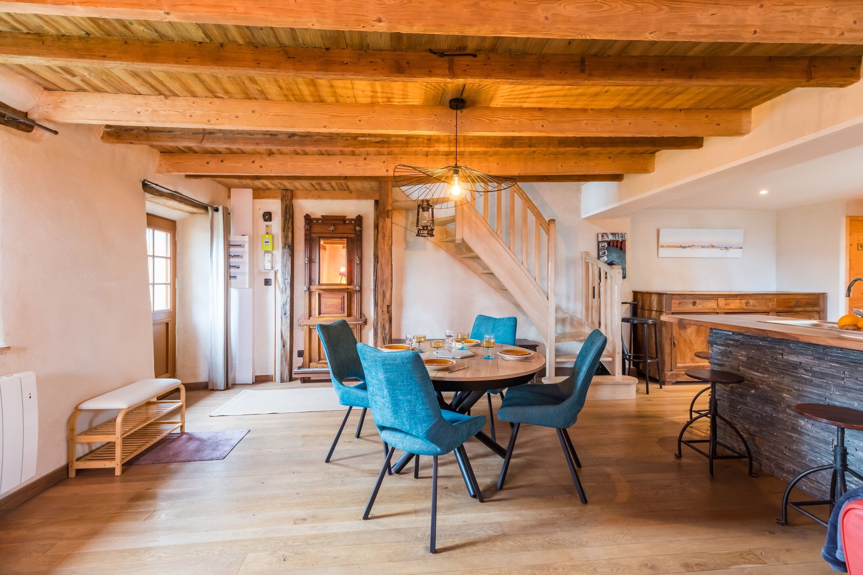 Un comedor con techo de madera, una mesa redonda con sillas y una zona de cocina con barra.