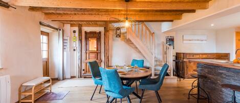 Un comedor con techo de madera, una mesa redonda con sillas y una zona de cocina con barra.