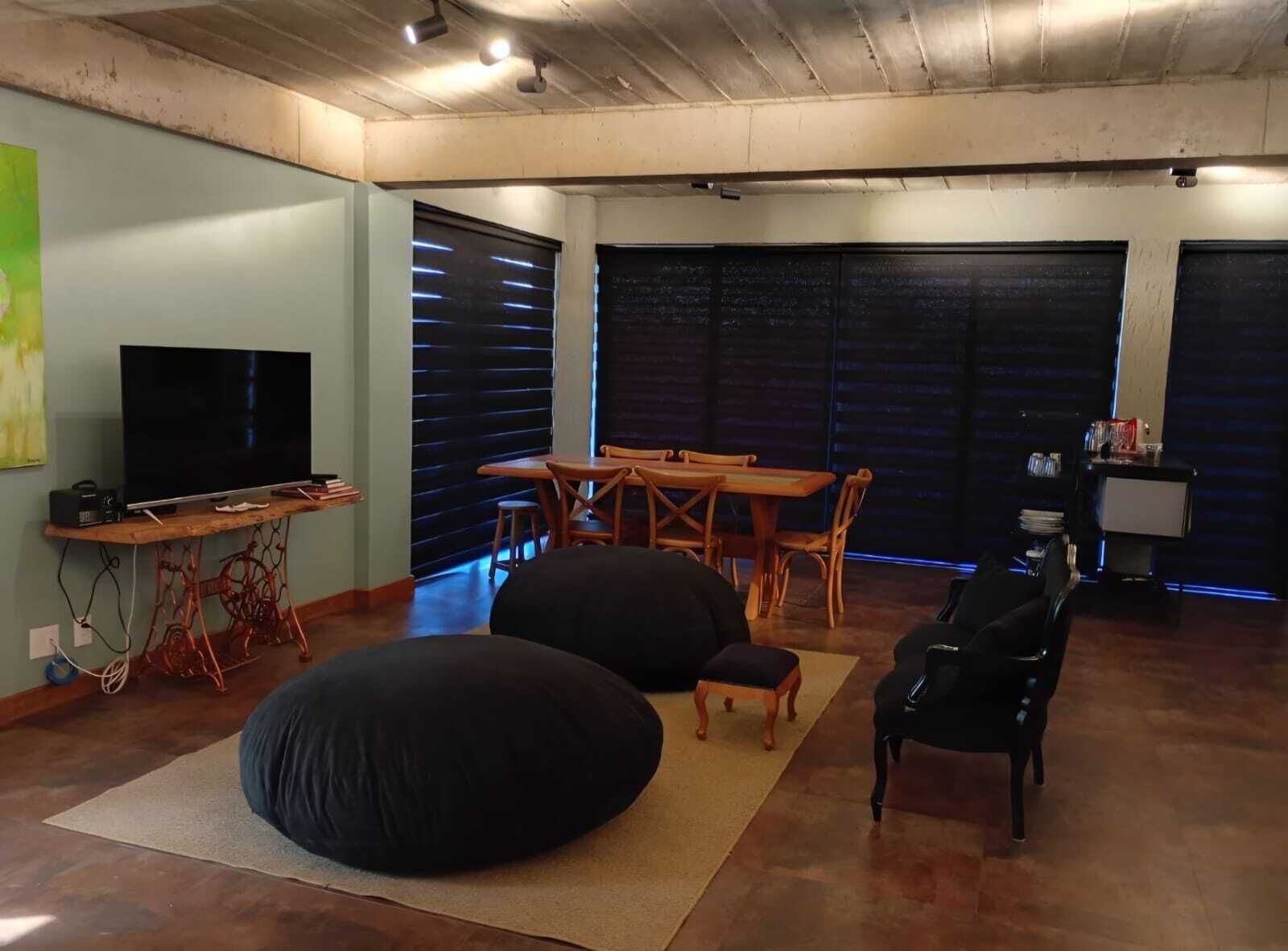 A living room with a television, a dining table, chairs, bean bags, and a small table with items on it.