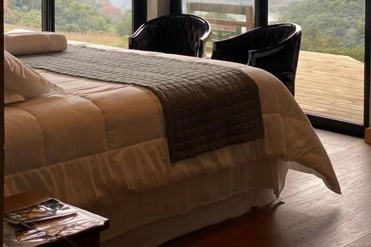 Une chambre dotée d’un grand lit, de deux fauteuils et offrant une vue sur un paysage montagneux grâce à de grandes fenêtres.