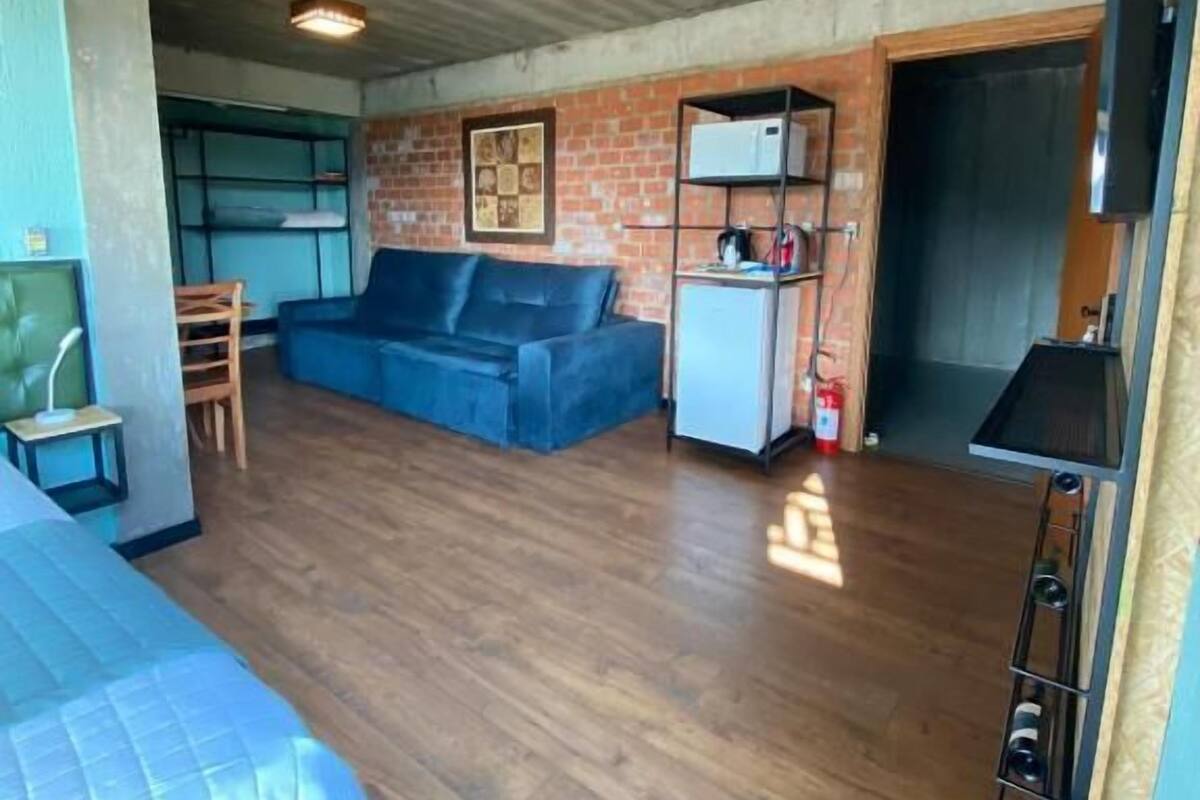 Un espace de vie compact comprenant un canapé bleu, une petite table, un coin cuisine et un mur en briques.