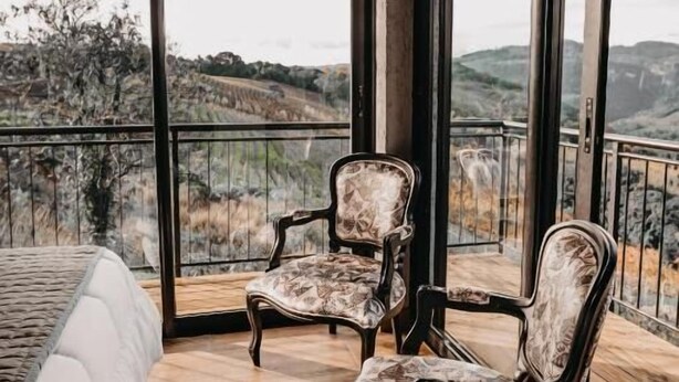 A balcony with two upholstered chairs and a bed, overlooking a mountainous landscape. - Pousada Refúgio dos Vinhedos (Vale dos Vinhedos)