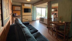 A spacious living area with a long dark-colored sofa, wooden dining table with chairs, and a kitchen area visible through an open door. - Pousada Refúgio dos Vinhedos (Vale dos Vinhedos)