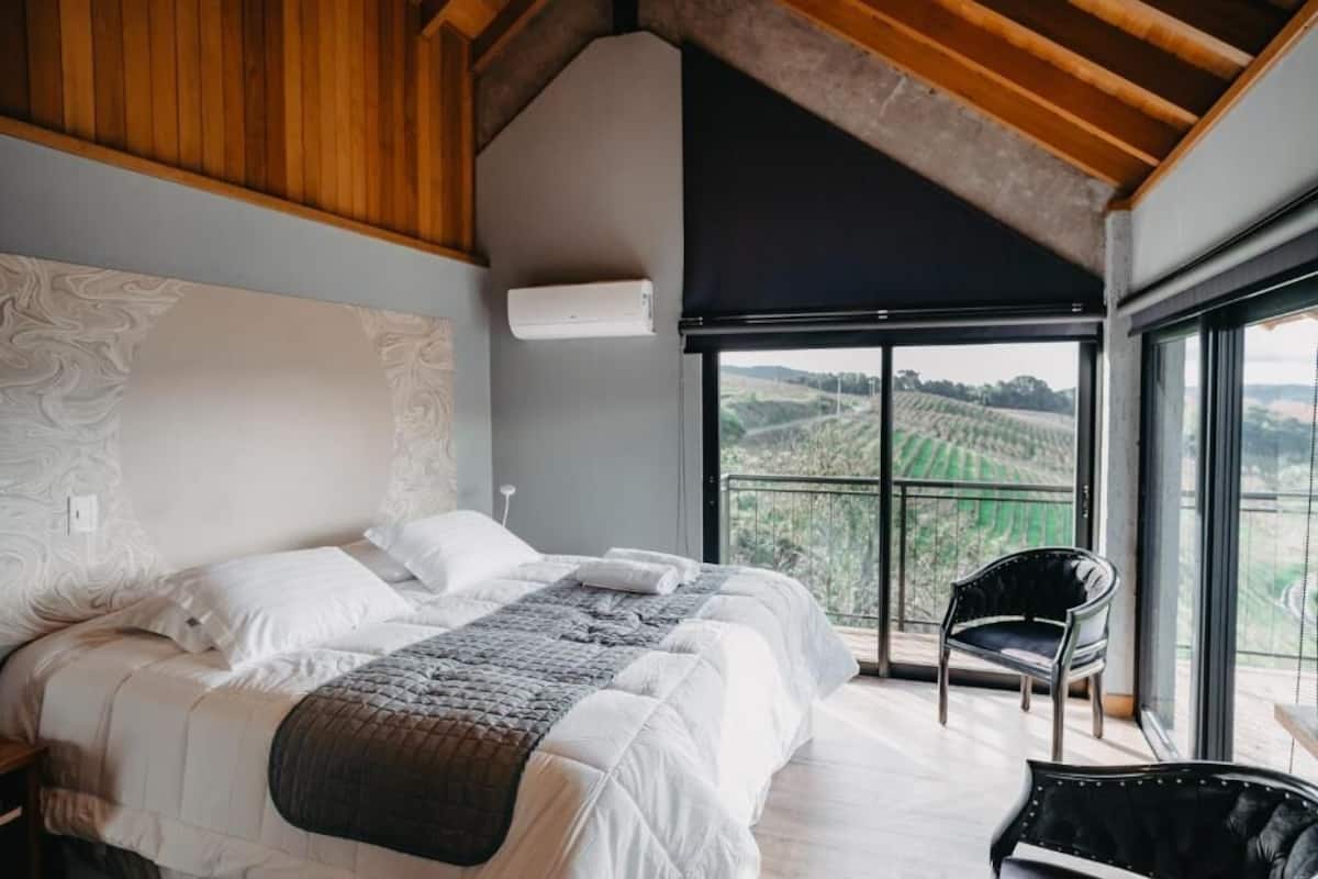 Une chambre avec un grand lit, une chaise et une vue sur des champs verdoyants, visible à travers de grandes fenêtres.