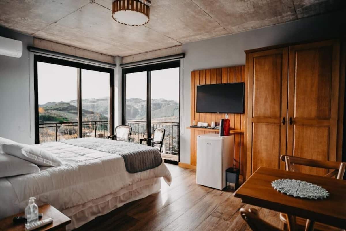 Une chambre avec un grand lit, une table en bois, une télévision et un balcon avec vue.