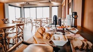 A dining area with wooden tables and chairs, a variety of food items on a buffet table, and a coffee machine. - Pousada Refúgio dos Vinhedos (Vale dos Vinhedos)