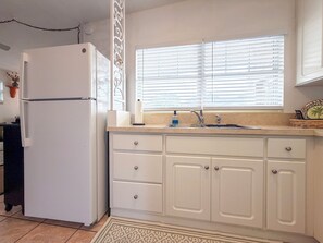 A kitchen with a refrigerator, a sink, and a window with blinds.