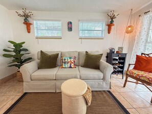 A striped sofa with pillows, a round ottoman, a potted plant, a wine rack, and a chair with a patterned cushion.