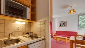 A kitchen with a microwave, stove, and dishwasher. There is a red sofa and a dining table with chairs in the adjacent living area. - Studio Cosy Près des Pistes!  Local à Skis (Les Deux Alpes (Isère))