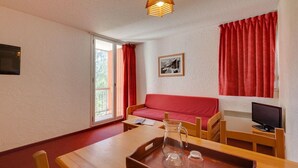 A cozy room with a wooden table, a red sofa, a television, and a window with red curtains. - Studio Cosy Près des Pistes!  Local à Skis (Les Deux Alpes (Isère))