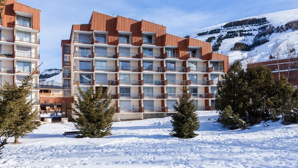 A multi-story hotel with balconies, surrounded by snow-covered ground and trees, with a mountain in the background. - Studio Cosy Près des Pistes!  Local à Skis (Les Deux Alpes (Isère))