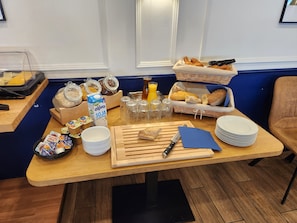 Una mesa de madera con una barra de desayuno buffet, varios alimentos, salsas y utensilios.