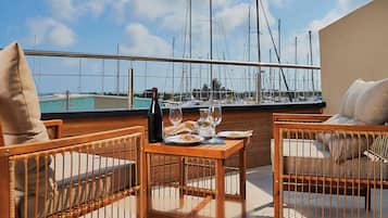 A terrace with wicker furniture, a table set with plates, glasses, and a bottle, overlooking a marina with boats.