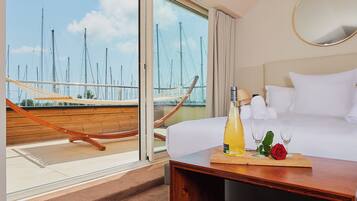 Une chambre d’hôtel avec un balcon, un lit, une table en bois avec une bouteille et un verre, et une rose rouge.