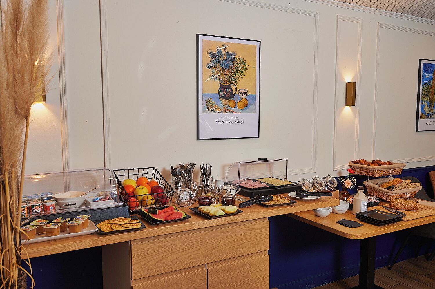 A breakfast buffet with various food items and utensils, a framed artwork on the wall, and a blue upholstered chair.