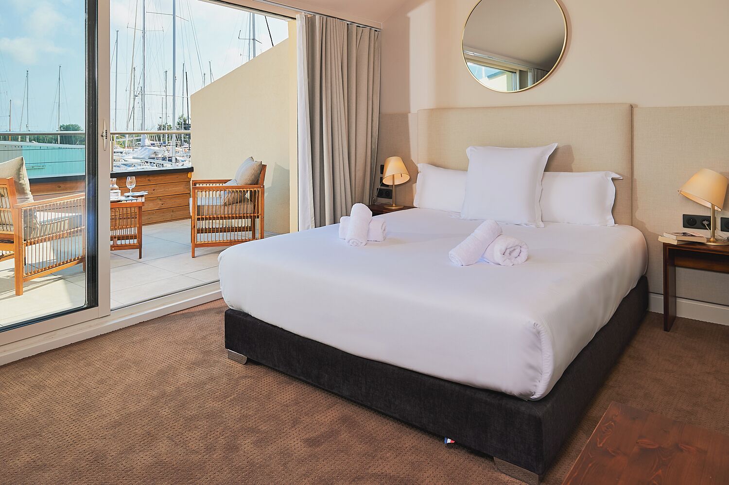 Ein Hotelzimmer mit einem großen Bett, einem Schreibtisch und Blick auf Boote durch eine Schiebetür.