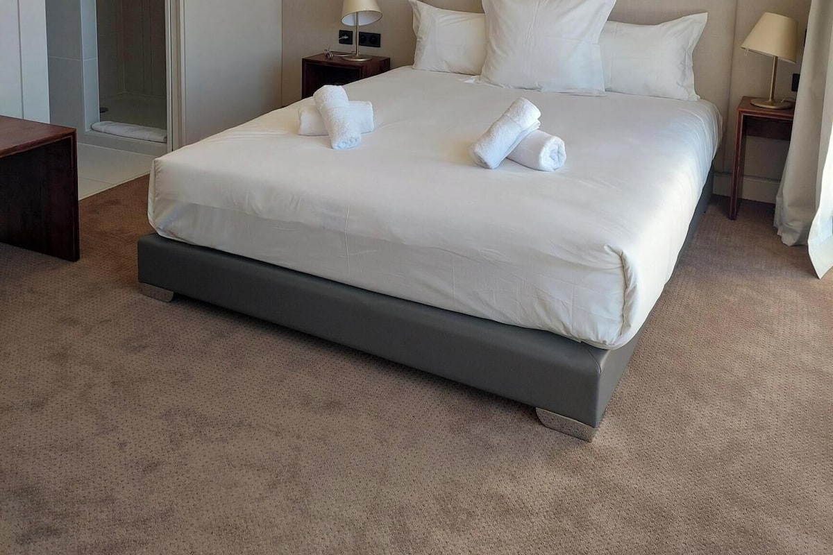 Ein Hotelzimmer mit einem großen Bett, zwei Nachttischen, einem runden Spiegel und einer Tür zu einem Duschbereich.