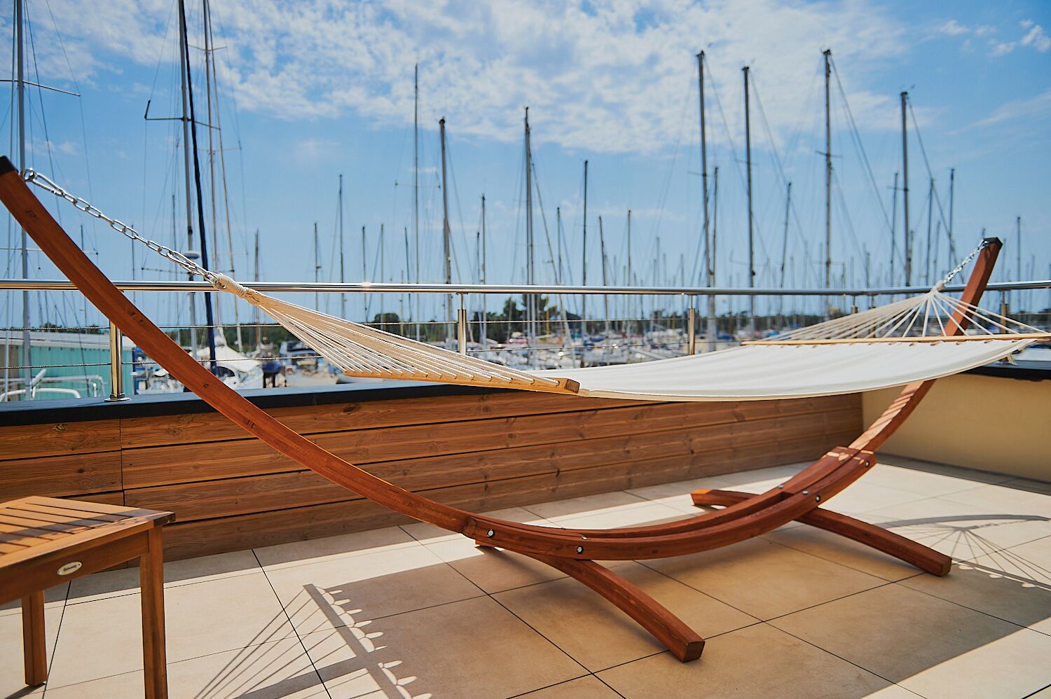 A hammock on a wooden deck with a view of sailboats in the background.