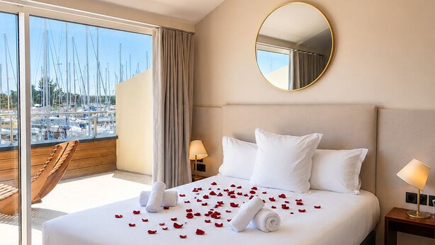 A hotel room with a bed, a round mirror, a view of boats through a large window, and a balcony. - Les Trois Voiles (Port-Saint-Louis-du-Rhône)