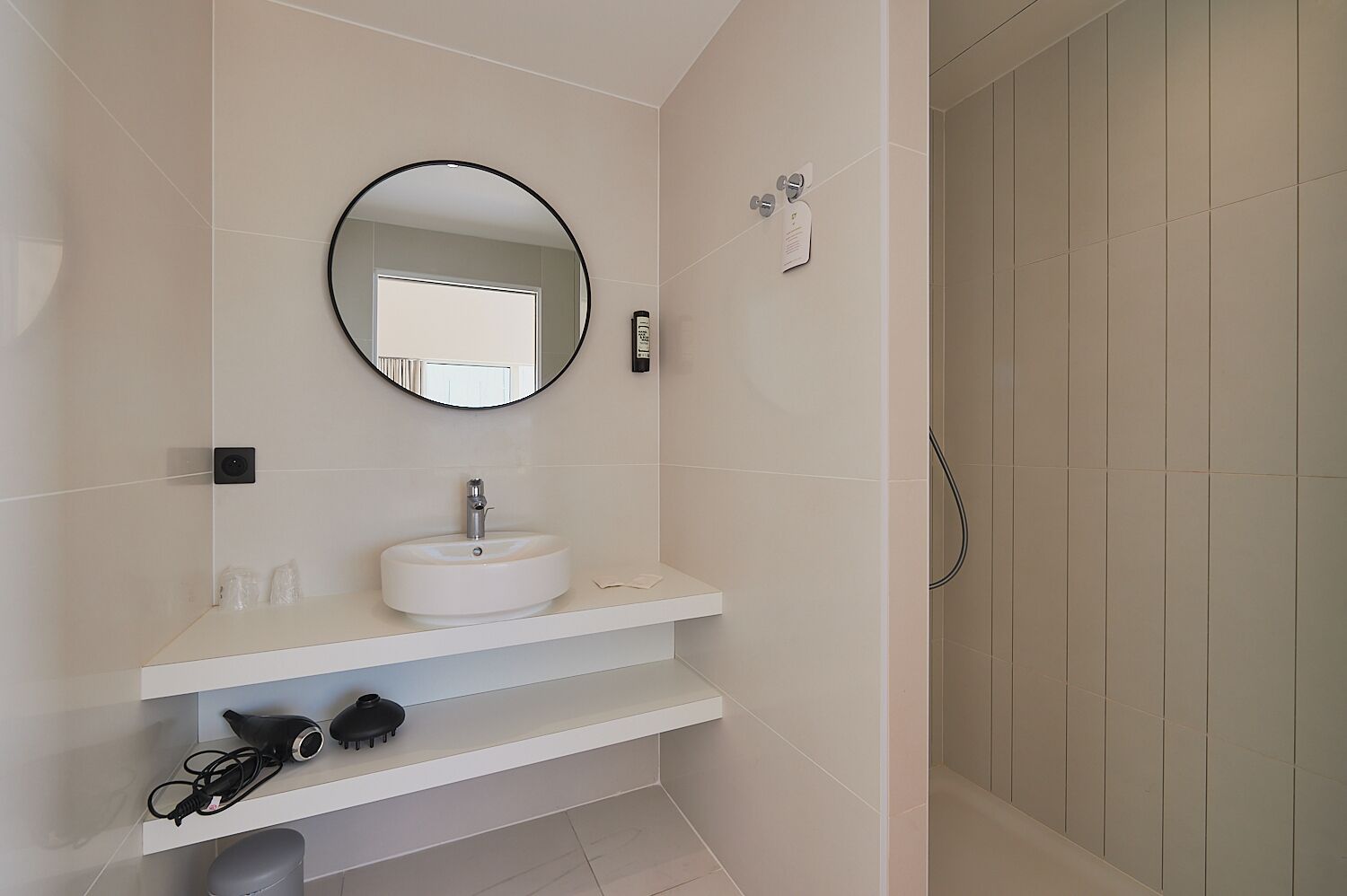 Un baño con lavamanos blanco, un espejo redondo y zona de ducha.