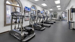 Ein Fitnessraum mit mehreren Landice-Tretmühlen, die in einer Reihe angeordnet sind, großen Fenstern mit Jalousien und einem Mülleimer auf der rechten Seite.