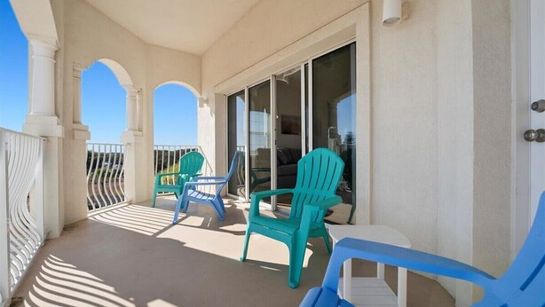 A balcony with chairs and a table, a sliding glass door, and a view of the sky. - Villas Of Ocean Gate II with Ocean View (St. Augustine)