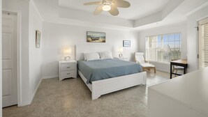 A bedroom with a bed, nightstands, a chair, and a window with blinds. - Villas Of Ocean Gate II with Ocean View (St. Augustine)