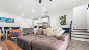 A modern living room with a sectional sofa, a wooden coffee table, and a dining area with a chair and table. - Modern home in Grand Prairie near DFW (Grand Prairie)