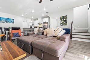Een moderne woonkamer met een hoekbank, een houten salontafel en een eethoek met een stoel en tafel.
