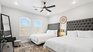 A bedroom with two beds, a ceiling fan, a large mirror, and a window with blinds. - Modern home in Grand Prairie near DFW (Grand Prairie)