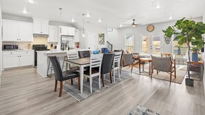 A modern kitchen with white cabinets, a central island, and a dining area with a wooden table and chairs. - Modern home in Grand Prairie near DFW (Grand Prairie)