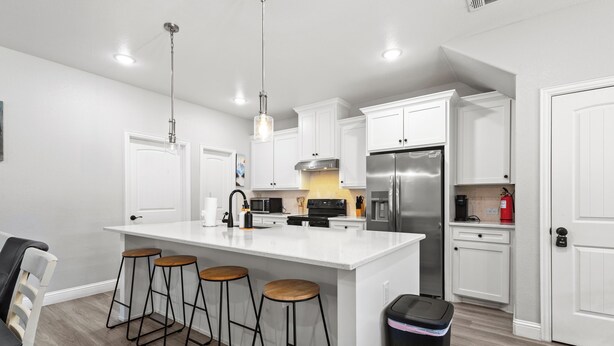 A modern kitchen with white cabinets, a stainless steel refrigerator, and a central island with stools. - Modern home in Grand Prairie near DFW (Grand Prairie)