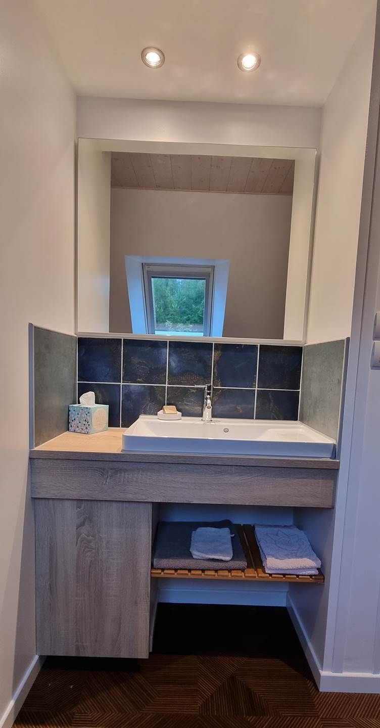 Ein Badezimmer mit integriertem Waschbecken, einem Fenster über dem Spiegel und einem Handtuchhalter darunter.