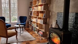 A cozy living room with a fireplace, a bookshelf, two chairs, a round table, and a large window. - "En Chemin" (LE FAOUET)