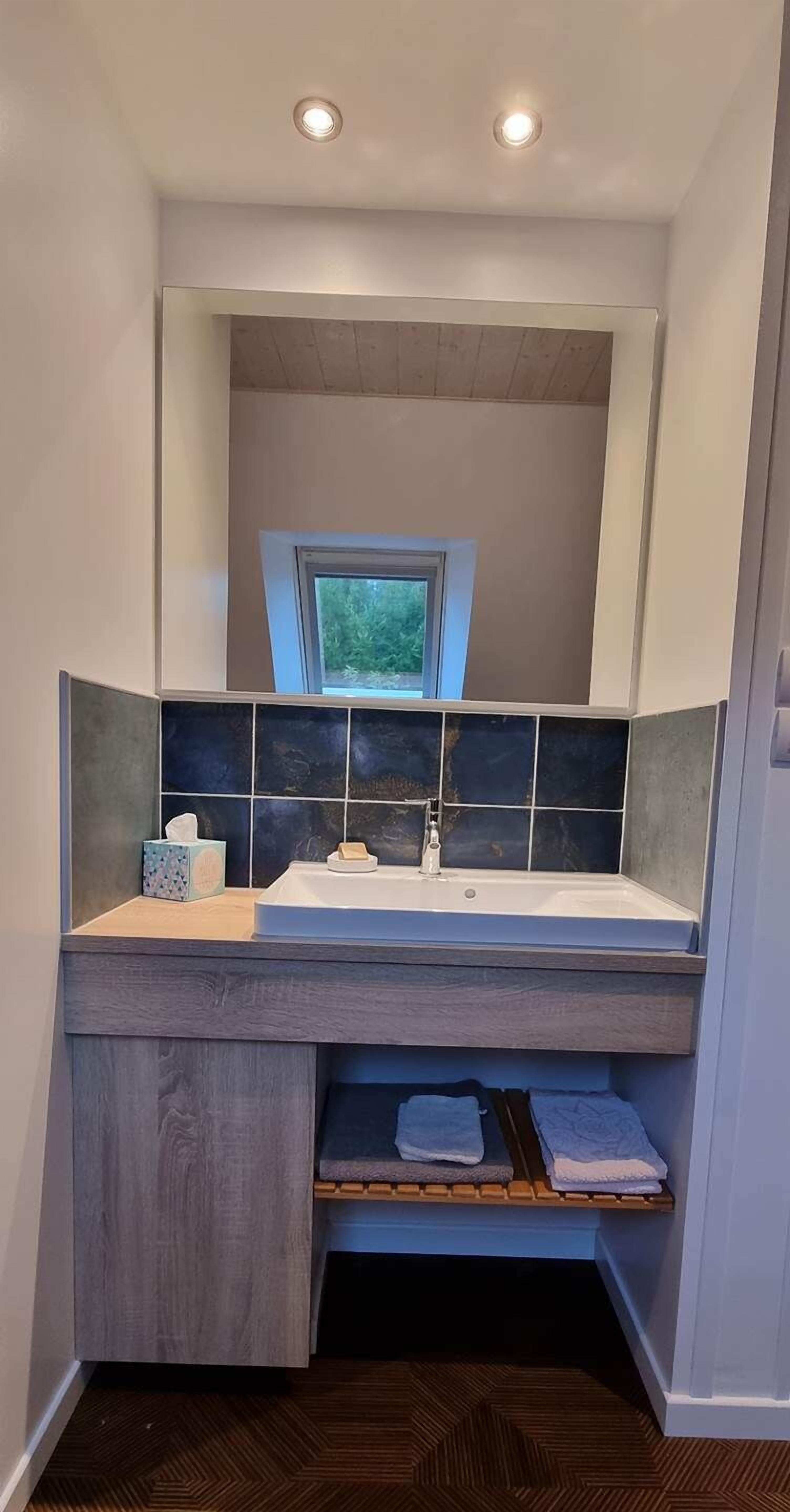 Une salle de bain avec un lavabo intégré, une fenêtre au-dessus du miroir et un porte-serviettes en dessous.